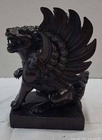 front left profile of dark-stained wooden griffin with spread wings on square base