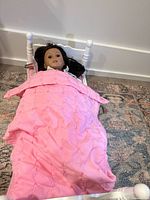 Doll lying in white bed with pink quilt