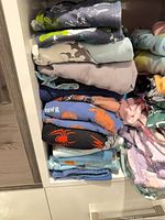 Left stack of folded boys’ pajamas showing dinosaur, shark, crab and solid prints