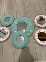 Five round wall mirrors laid out on floor showing frame colors and styles