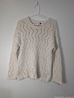 Full front view of cream open-knit sweater on hanger