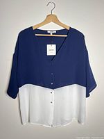 Front view of navy and white color-block blouse on hanger showing V-neck, buttons, hangtag