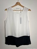 Front view of Tahari white blouse with black bottom panel on hanger