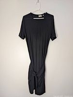 Front view of black Wilfred Free dress on hanger, showing tie waist detail
