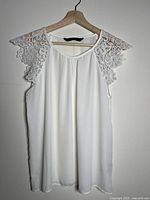 Front view of white tank top on hanger showing lace cap sleeves and draped body