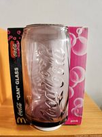 Purple tinted Coca-Cola can glass partially removed from pink box