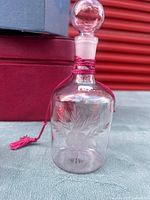 Clear glass perfume bottle with etched design and stopper, magenta cord visible