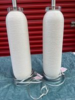 Two cream cylindrical lamps with cords coiled at bases