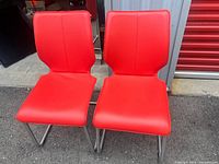 Front view of both Bree's New World red chairs showing upholstery and metal sled bases