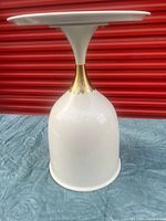 Full view of white pedestal side table showing goblet form and bronze neck accent