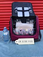 Tote open displaying wrapped utensils, plates, wine glasses and sign