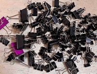 Pile of black binder clips assorted sizes on tabletop