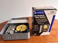 Open gray metal time switch with yellow dial alongside Intermatic T103 box