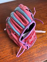 Side view of pink Rawlings glove showing finger padding, teal accents, laces