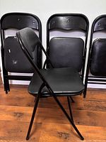 Side view of unfolded chair with three folded chairs behind showing frame style, padding and wear