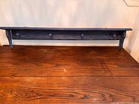 Front view of blue wooden peg shelf showing four pegs and top ledge