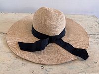 Top view of natural straw wide-brim hat with black ribbon bow