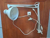 White IKEA adjustable desk lamp with cord, clamp and wall mount plate laid flat