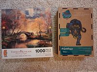 Both puzzle boxes: Thomas Kinkade 1000-piece Central Park in the Fall and Puzzle Art 200-piece Panther