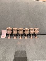front view of six pewter goblets standing in a row
