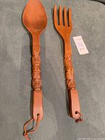 Front view of carved teak spoon and fork with tiki faces, leather cords visible