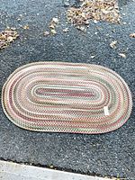 Full view of oval braided rug on asphalt surface