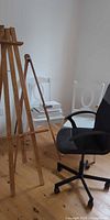 Overall view of both easels, white chair, black swivel chair and canvases