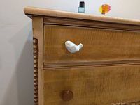 Left front corner showing top drawer with white bird knob and bead column