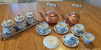 Group shot showing teacups, saucers, copper kettles, Delft canisters in basket