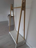 Full view of garment rack angled side showing wood frame, hanging bar and white slatted shelf