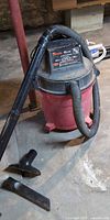 Full view of Shop-Vac canister vacuum with hose, wand and two nozzle attachments on floor