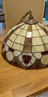 Full view of stained glass ceiling lamp shade resting on table, chain visible