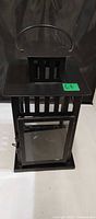 Front view of black IKEA metal lantern showing glass door, handle and slatted top