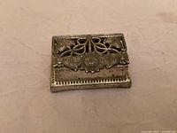 Front view of ornate metal stamp box closed