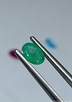 Emerald gemstone held by tweezers, showing oval cut and green color