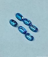 Six faceted oval blue topaz gemstones shown on neutral background
