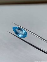 Blue topaz held by tweezers, profile view of pear shape