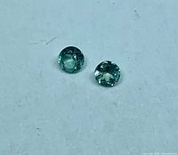 Two light green round Alexandrite stones on white background