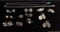 All items laid out on black background, showing necklaces, earrings, cufflinks, brooch