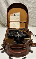 Camera and accessories inside open leather case with paperwork in lid