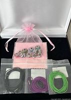 Overall view: three bagged lariat cords and charms in organza pouch