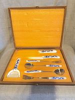 Open wooden presentation box showing seven utensils set in orange padded interior