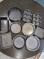 assorted pans laid out on table: loaf, springform, muffin tins, round, square