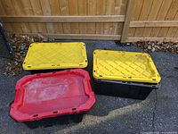 Three hard plastic totes: two with yellow lids, one with red lid