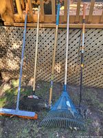 All five lawn care tools standing against lattice fence
