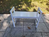 White bench style shoe rack on outdoor patio, shows overall structure and color