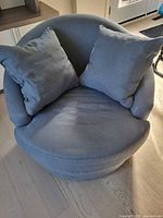 Front view of light blue-grey round swivel chair with two matching pillows