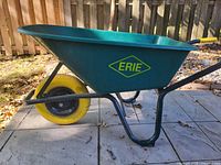 Left side view of green Erie wheelbarrow showcasing yellow flat-free tire and steel frame