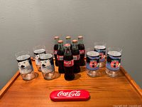 All items on wooden surface: six glasses, holiday bottles, red tin