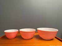 Three pink Pyrex bowls in nesting order on wooden surface